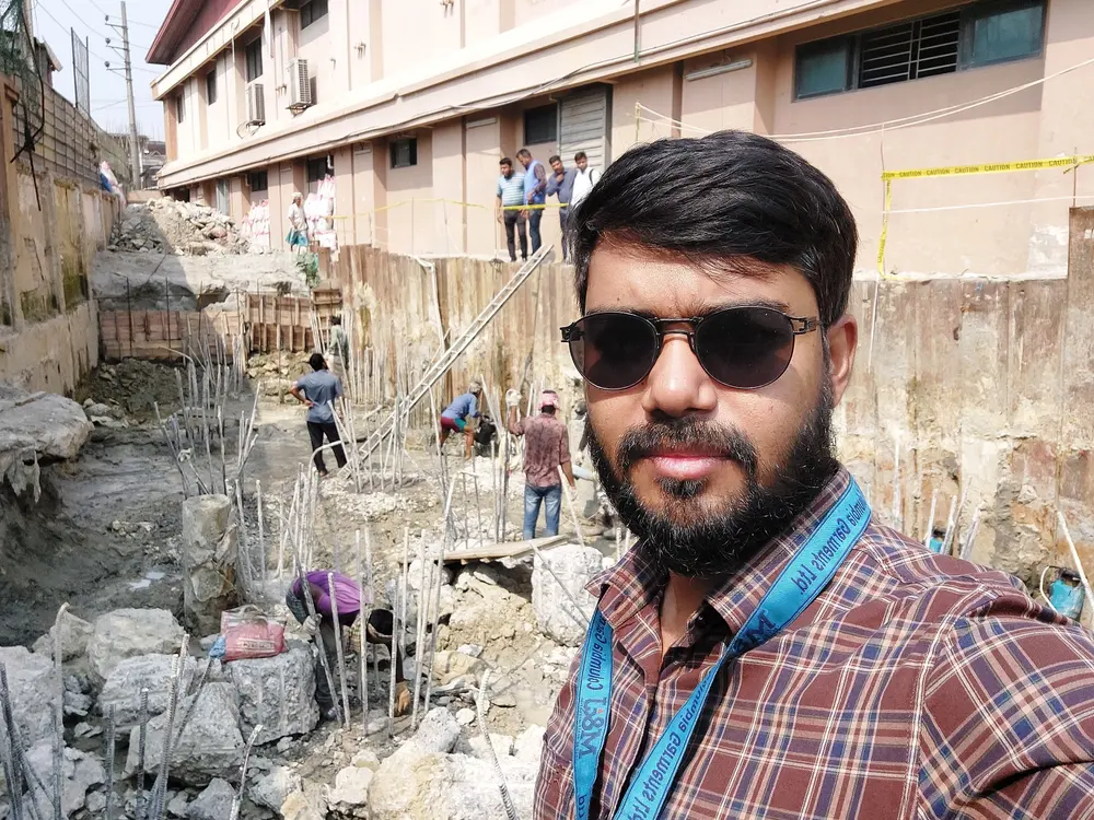 Engineer in sunglasses at an excavation with sheet piles and rebar beside a factory building